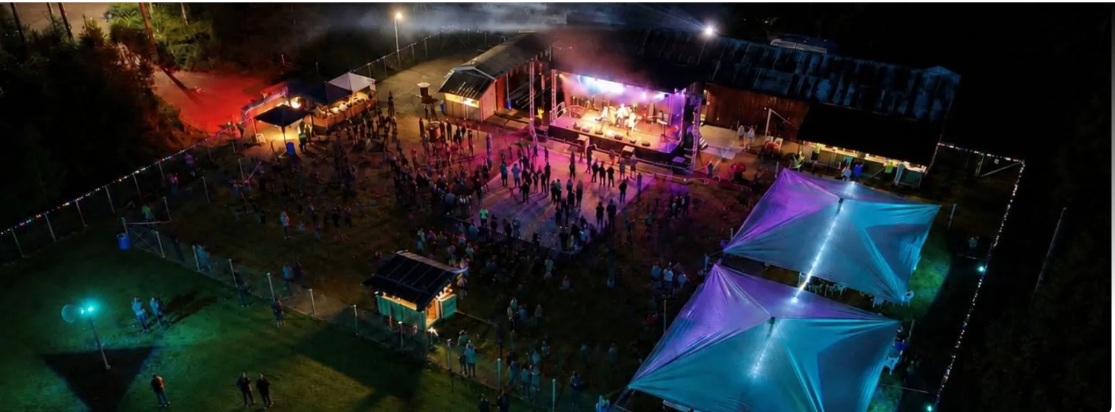 Festivalplatsen i Östmark fotograferad från ovan en sommarkväll – upplyst scen, publik på dansbanan, serveringstält och festivalområdet under tak.
