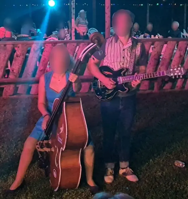 Rockabillyduo med kontrabas och elgitarr spelar på gräset framför publiken en sommarnatt.