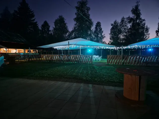 Serveringsytan med vita tält, ljusslingor och trästaket i blått kvällsljus.